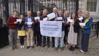Group of people stood outside number 10 downing street in front of black gate holding envelopes and a flag reading Making Space for Water