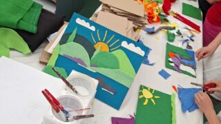 A craft table is strewn with brightly coloured offcuts of felt, and river designs created by children