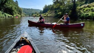 View from a canoe on a river looking two people paddling in a different canoe