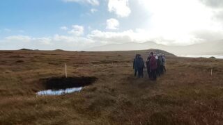People stood next to pool of water on a peatland with hills in the background