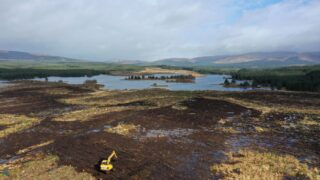 Ariel view of a peatland with a yellow digger in the foreground and a river in the background