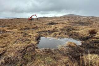 Pool of water on a peatland in the foreground and a digger in the background