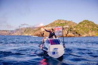 Man on rowing boat in the sea holding a red flare with hills in the background
