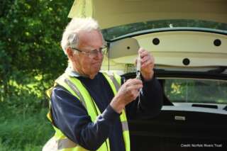 Old white man in high visibility jacket stood holding a test tube