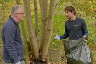 Young man on the right holding a rubbish bag and gesticulating with his right hand while chatting to an older gentleman in the woods