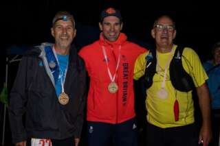 Three men stood in the dark each with a medal around their neck