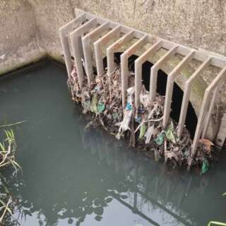 A sewage outlet into water showing debris and litter in the grates