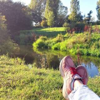 Feet up crossed wearing ping trainers with a river in the background