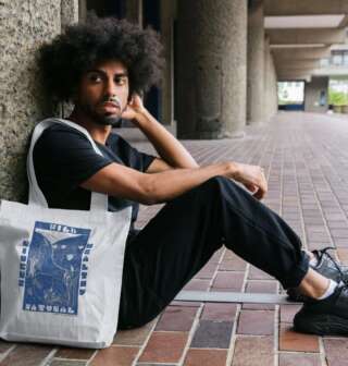 A man sits on the floor holding a white tote with bold blue river design