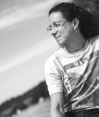 A smiling woman looks over a river in greyscale
