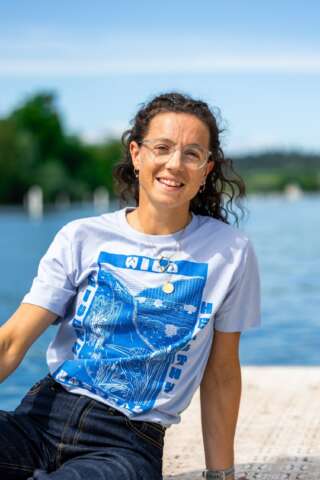 A smiling woman sits on a dock overlooking a river