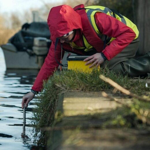 Person in waterproof jacket and high vis vest using a test tube to monitor a river