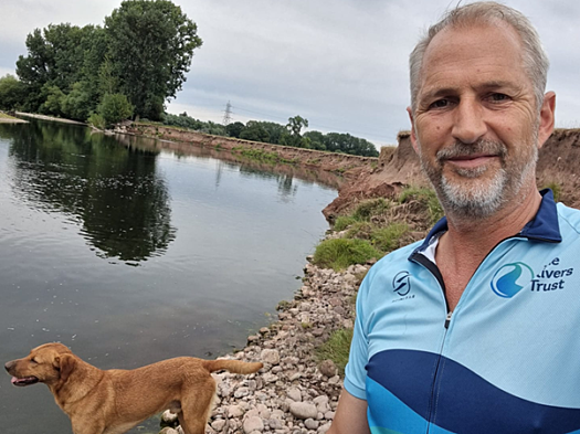 A man and his brown dog stand in front of a river in running gear