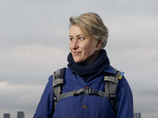 A smiling woman stands on the foreshore of the thames