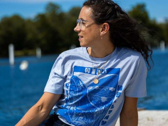 Imogen Grant sits on a dock by the river wearing a light blue tee with stylish dark blue river design