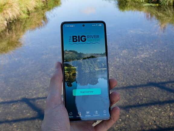 Hand holding a phone with an app reading Big River Watch with a river in the background