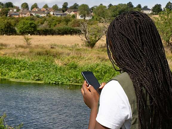 View of the shoulder of a young black female teenage holding a phone looking at a river