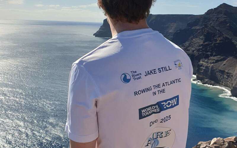 Photo from behind of a man stood overlooking a bay of water from a cliff.