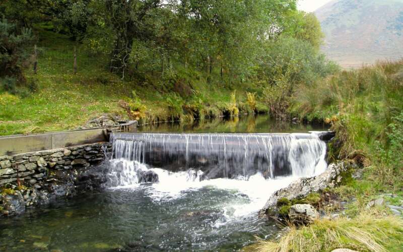 Water falls over a tall weir stretching across a river