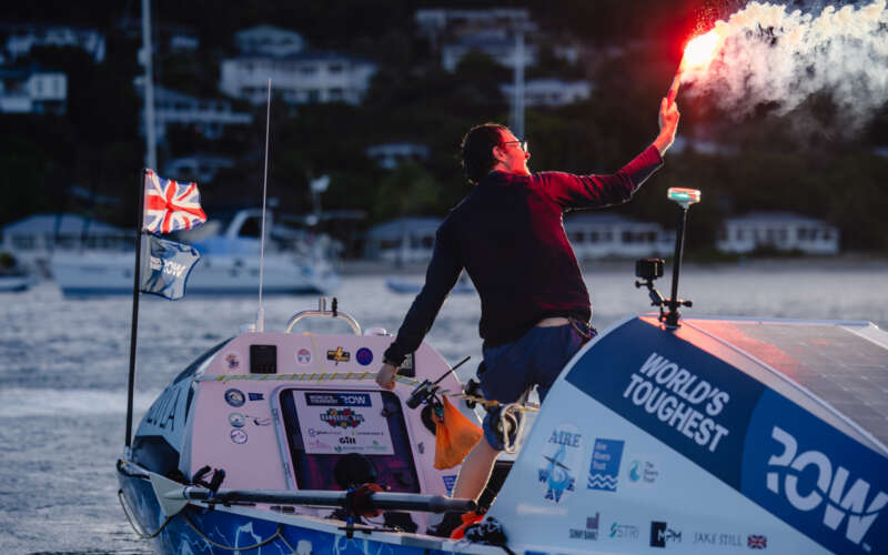 Man stood up holding flare on boat pulling into harbour