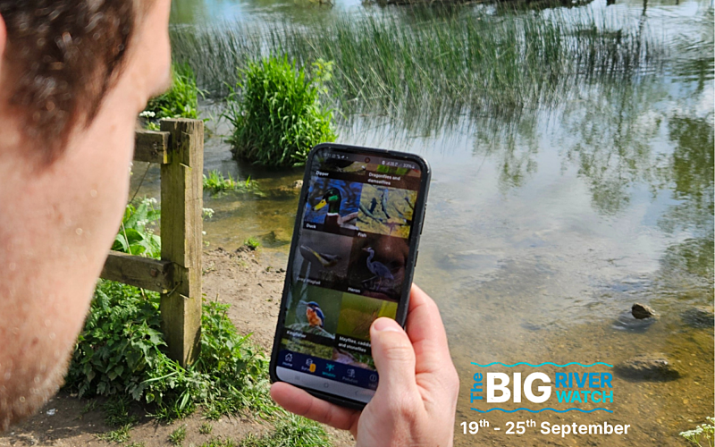 View over man's shoulder holding phone up in front of a river