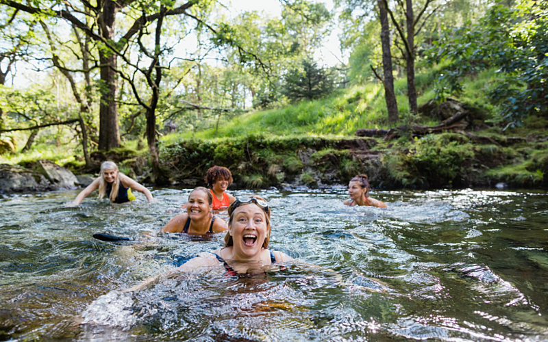 People swimming in river and smiling with trees in background.