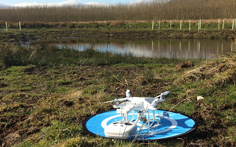 White drone sat on blue landing pad in a green field with water in background
