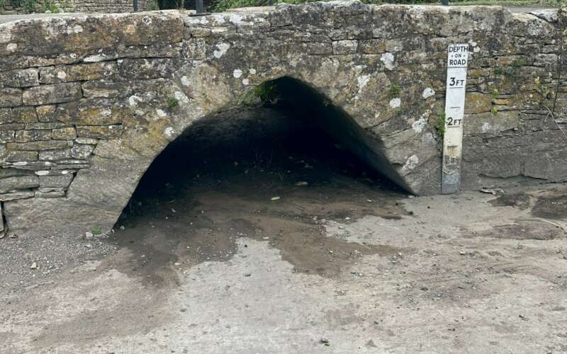 a bridge over a dried up river ford is shown with a height marker to one side