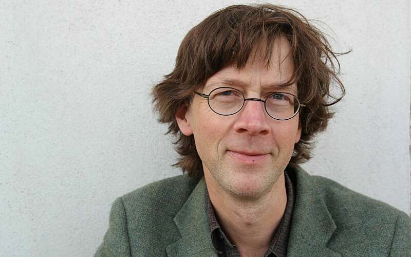 A man looks at the camera, with round glasses and brown hair