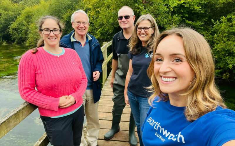 five smiling people stand on a bridge facing the camera