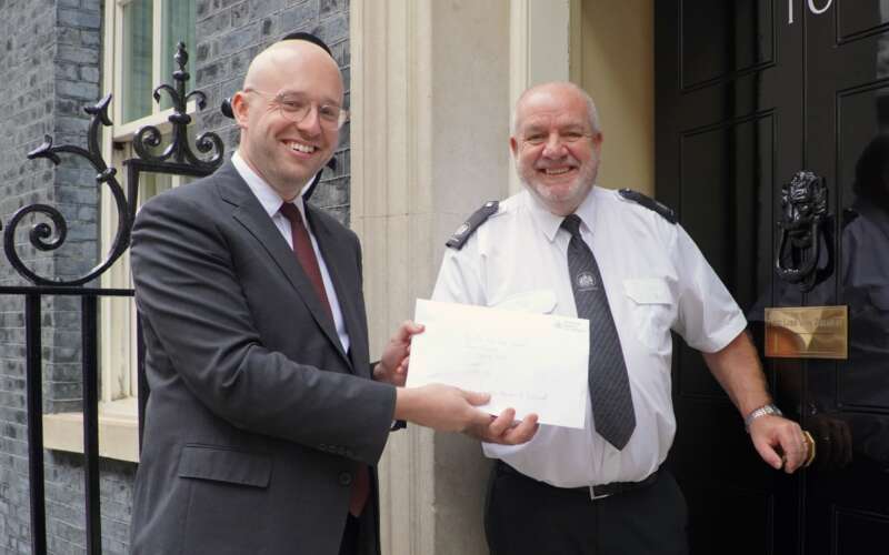 Bals white man in black suit and red tie handing a letter to a bald white man in white shirt and black tie in front of black door with number 10 on it