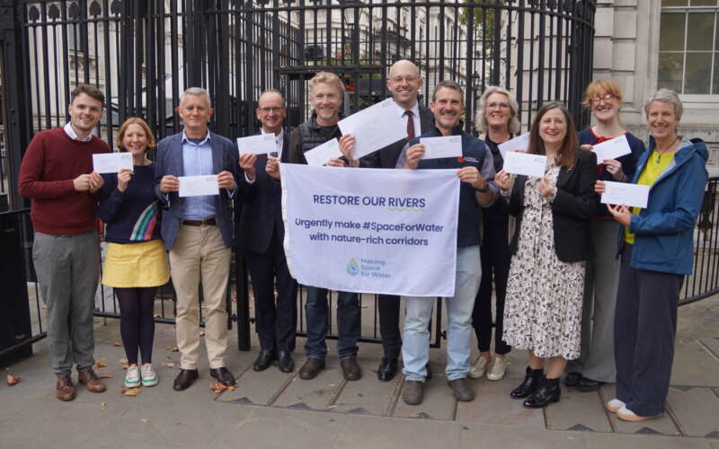 A group of people stood in front of black gates holding a white flag and envelopes