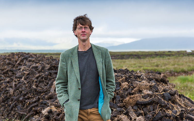 White man stood outside with grass behind him and blue sky