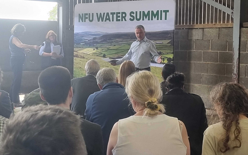 People in foreground attending a talk in a barn with a banner above the presenter reading NFU Water Summit.
