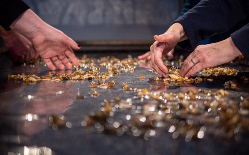 Two pairs of hands gathering small orange petals on a table