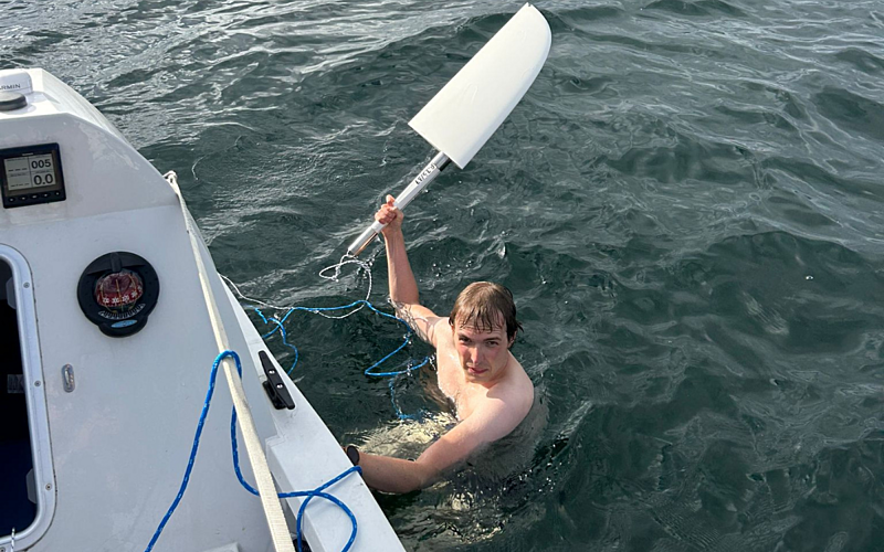 Topless man in the sea next to a rowing boat holding a rudder