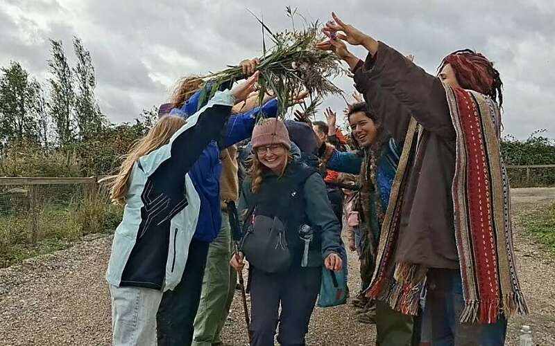 a smiling woman walks through an arch of arms held up by a welcome party at the end of her walk