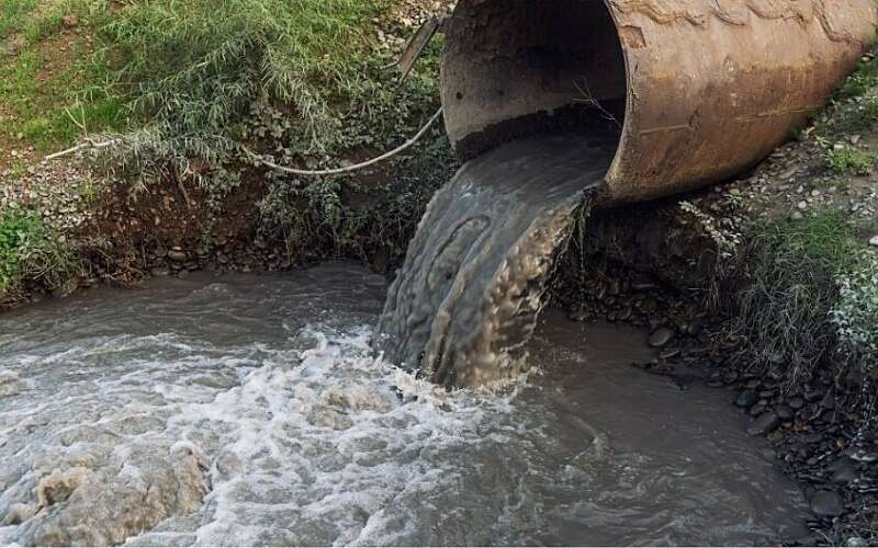 Disgusting brown water pours out of a meal pipe into a river