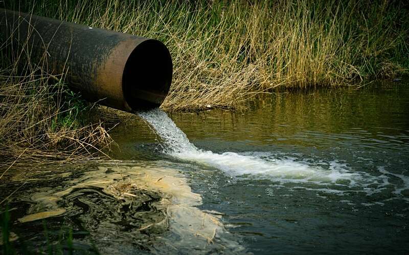 liquid pouring from a pipe into a river leaving a pale film on the water surface