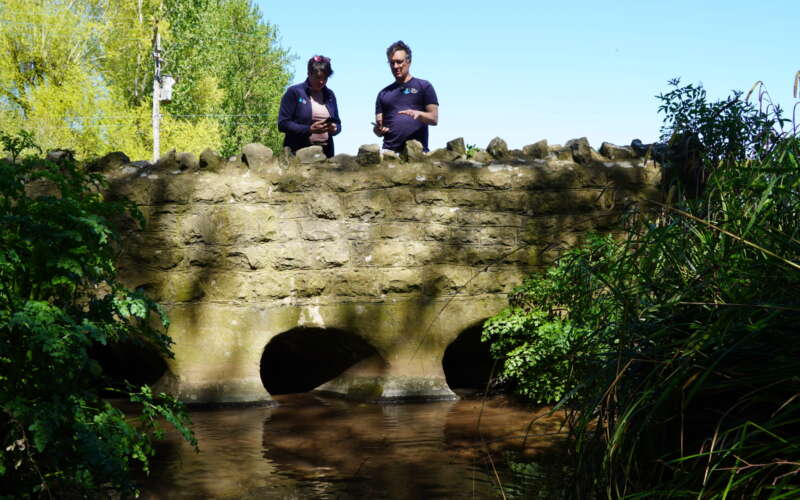 Man and woman stood on a stone bridge over a river