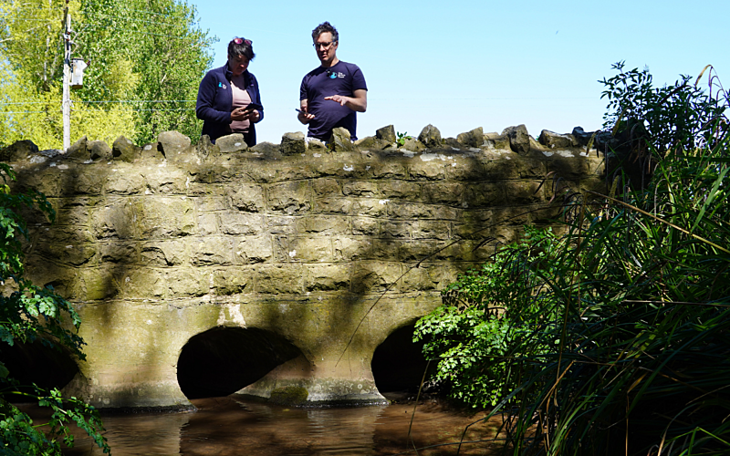 Man and woman stood on stone bridge overlooking river