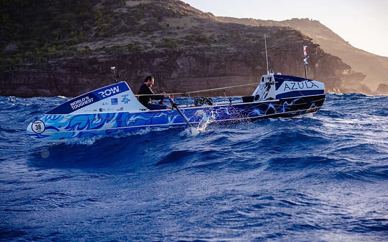 Man on rowing boat in ocean with land behind him