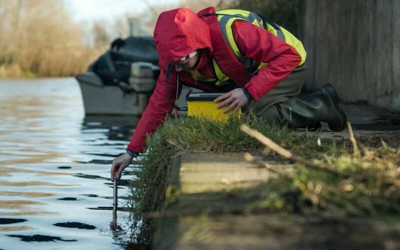 Person in waterproof jacket and high vis vest using a test tube to monitor a river