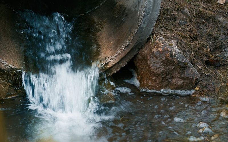 Water rushes out of a dirty pipe into a river