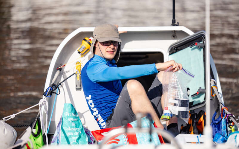 Man in blue shirt on row boat surrounded by supplies