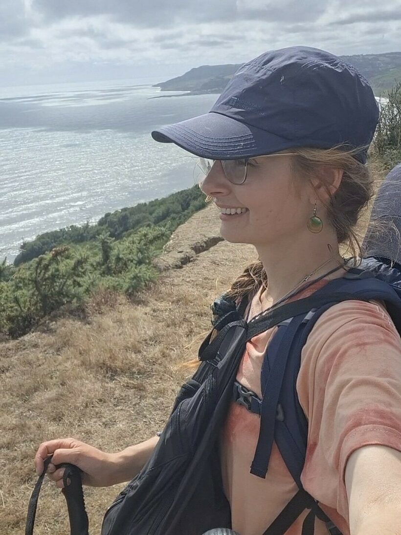 a smiling woman in a baseball cap looks over a river
