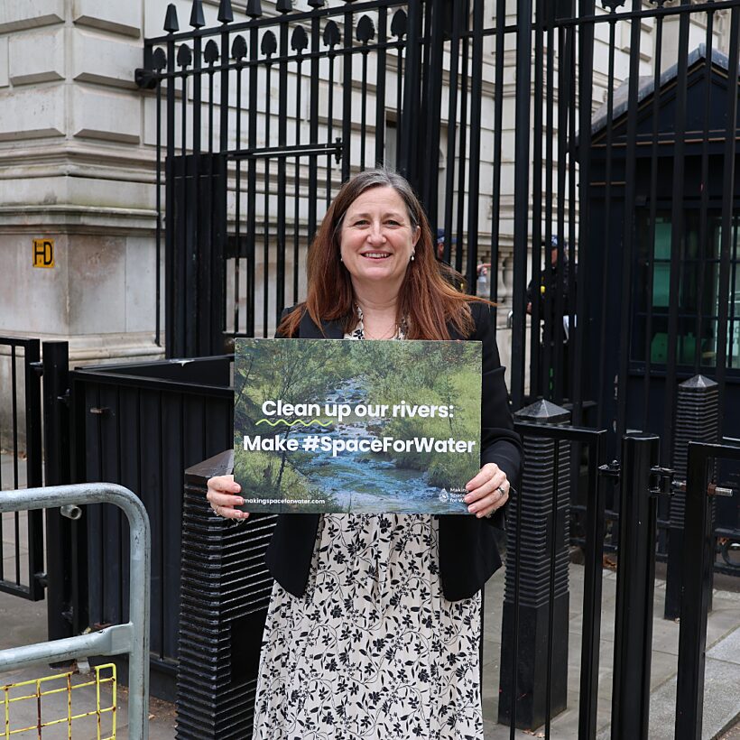Woman stood in front of black gate holding a sign