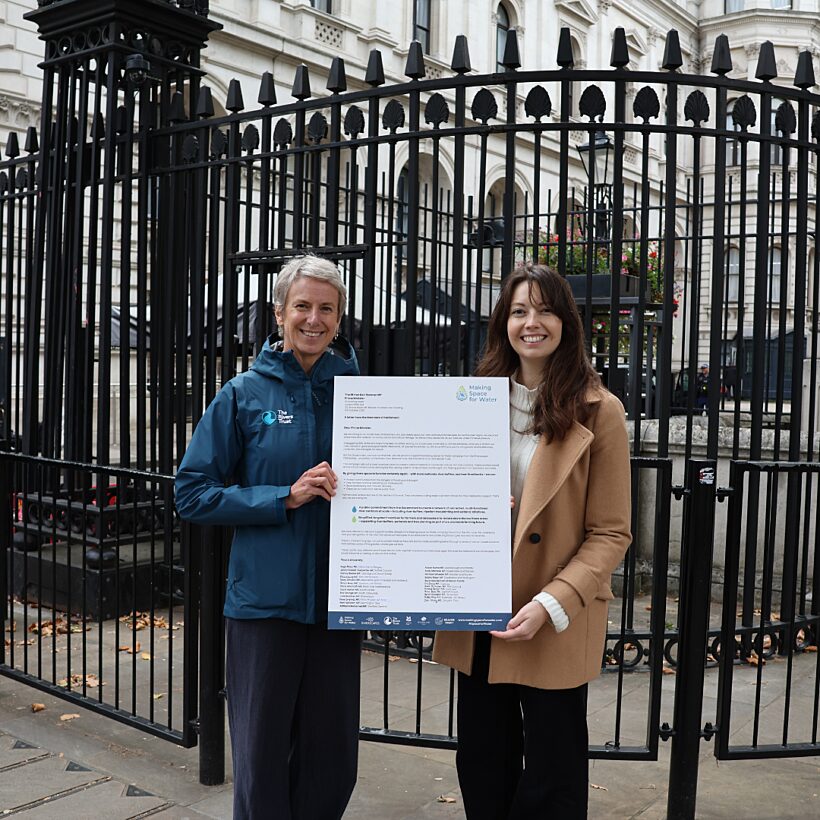 Two women stood in front of black metal fence holding large A3 printed letter