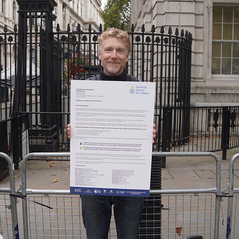 Man stood in front of black metal fence holding large A3 printed letter