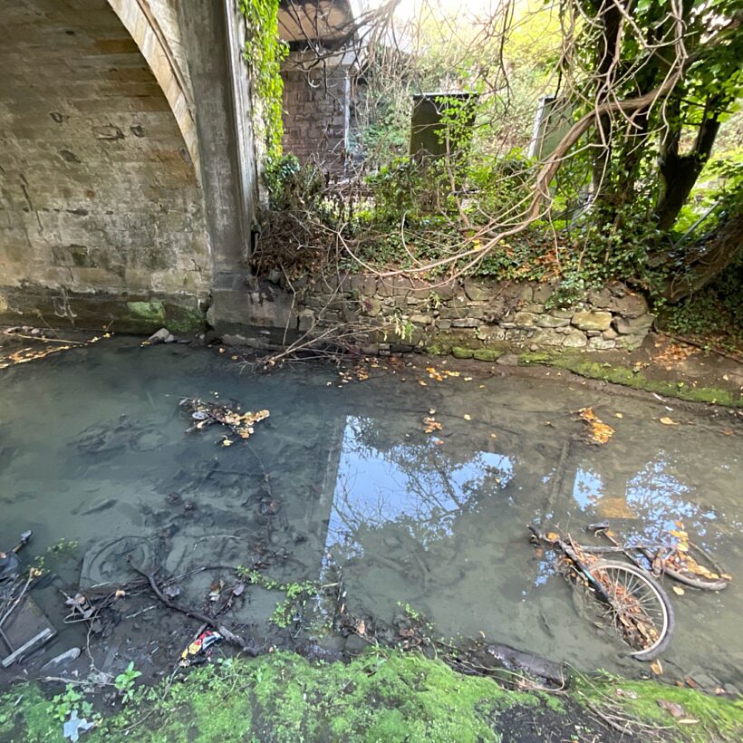 A river running under a bridge with murky water and a bike in the water